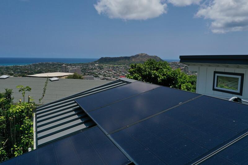Black solar panels on a standing-seam metal roof at an Oʻahu home, with Honolulu and Diamond Head in the distance.